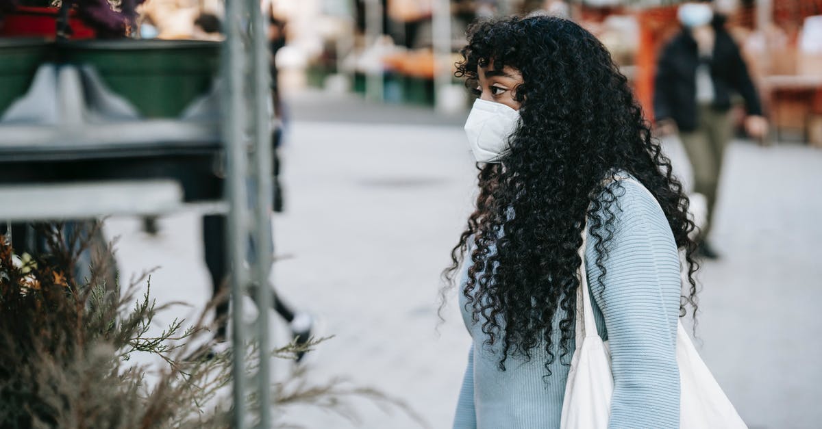 How to pick a good mango at a local store? - Black woman in respirator choosing potted flowers on street market How to pick a good mango at a local store? - Black woman in respirator choosing potted flowers on street market