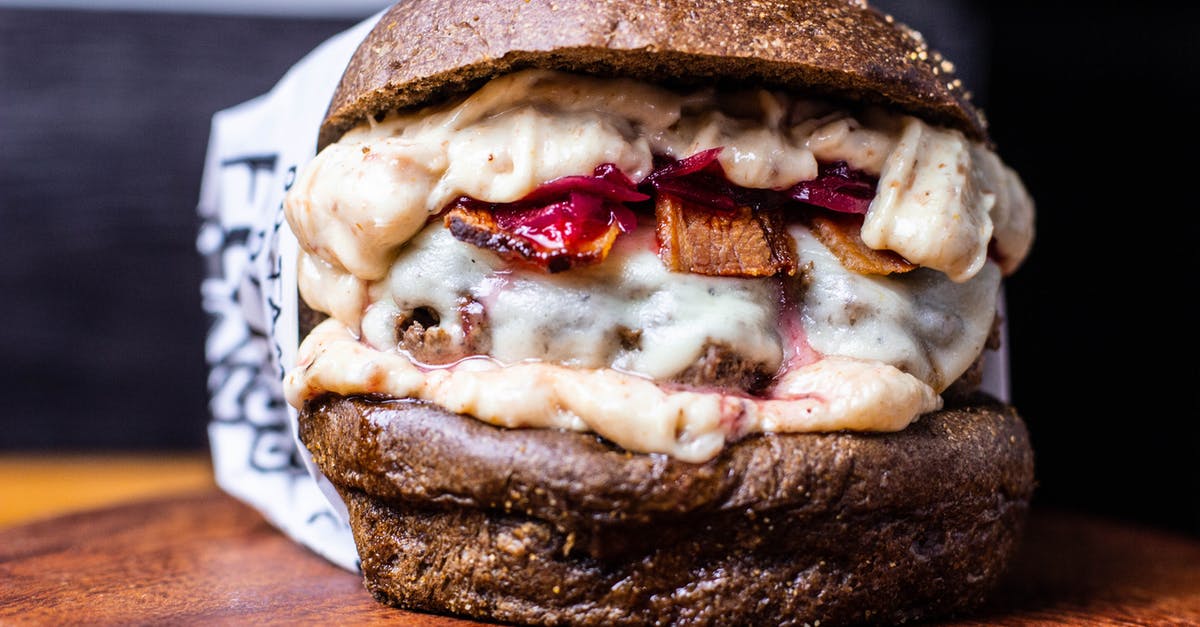 How to prepare an easy and fast snack rich in protein? [closed] - Closeup of appetizing hamburger with cheesy sauce and black bun placed on wooden board in cafe