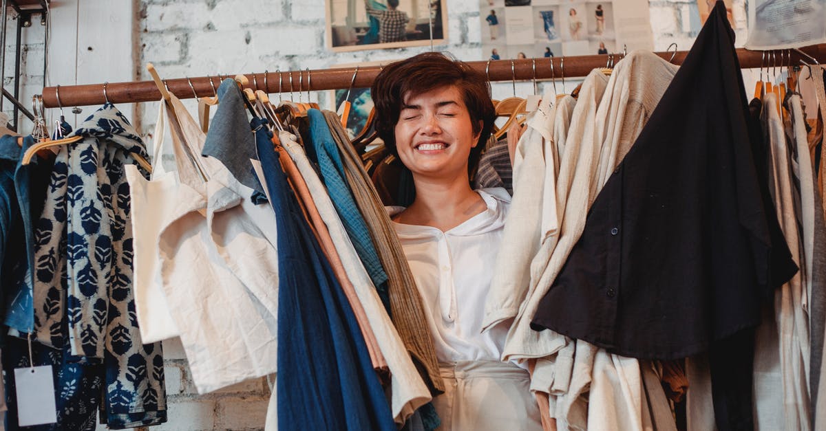 How to select a drain rack for pots and pans? - Cheerful Asian female customer standing among hanging clothes in store and smiling How to select a drain rack for pots and pans? - Cheerful Asian female customer standing among hanging clothes in store and smiling