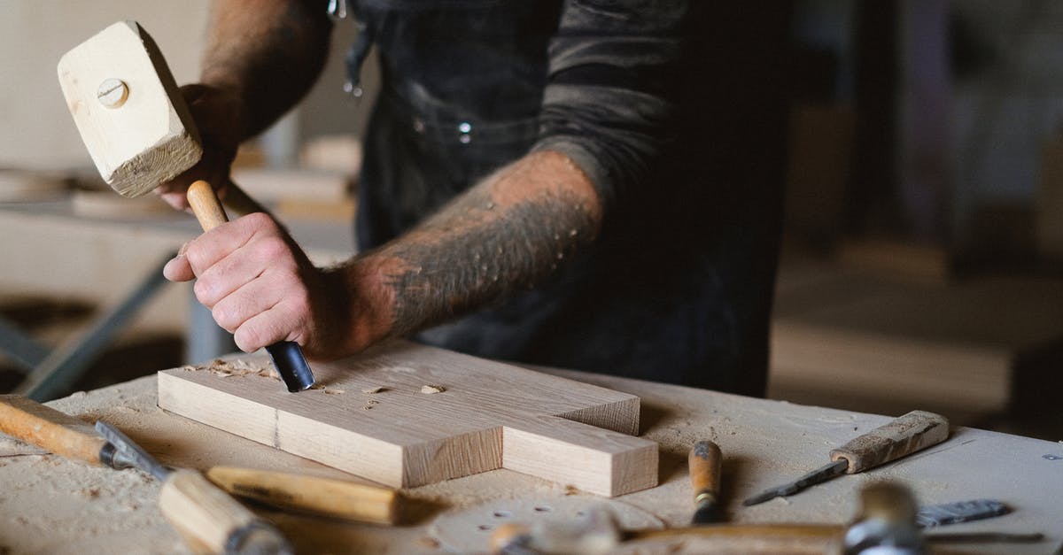 How to shell macadamias without a special tool? - Unrecognizable male carpenter using forged chisel and wooden hammer while creating pattern on lumber board at table in workshop on blurred background How to shell macadamias without a special tool? - Unrecognizable male carpenter using forged chisel and wooden hammer while creating pattern on lumber board at table in workshop on blurred background