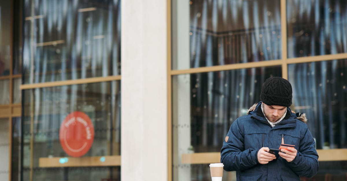 How warm must dough be in order to rise? - Focused young male in warm outerwear and hat standing near modern building with takeaway coffee and using smartphone while making online shopping with credit card How warm must dough be in order to rise? - Focused young male in warm outerwear and hat standing near modern building with takeaway coffee and using smartphone while making online shopping with credit card