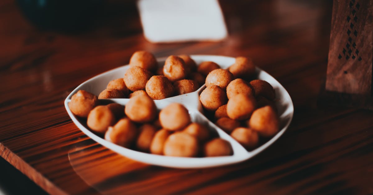 Identify this unusual spicy appetizer - Roasted salty nuts on white plate served on table Identify this unusual spicy appetizer - Roasted salty nuts on white plate served on table