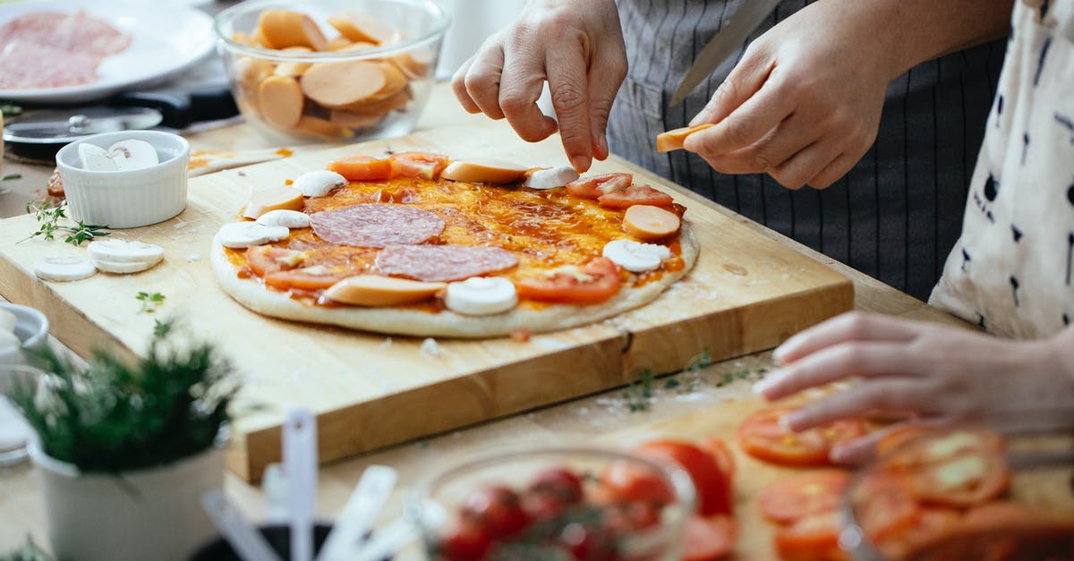 In a tomato sauce recipe, how can I cut the acidity? - Crop anonymous person in apron adding sausages on pizza with salami and champignons while cooking in kitchen In a tomato sauce recipe, how can I cut the acidity? - Crop anonymous person in apron adding sausages on pizza with salami and champignons while cooking in kitchen