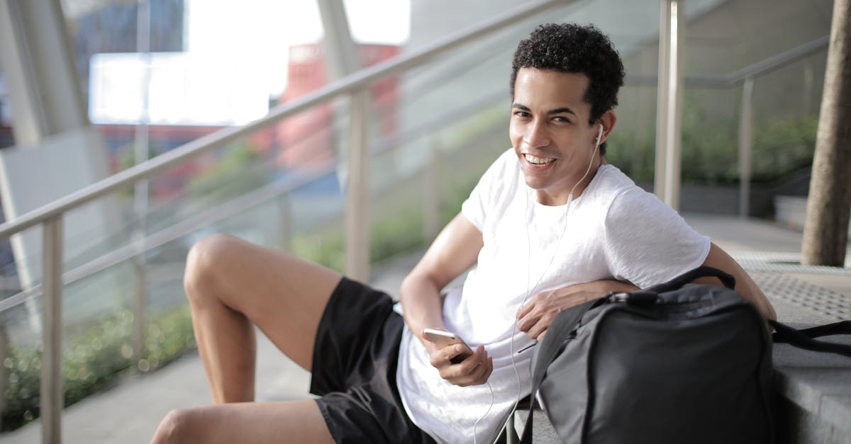 In what situation could we use black garlic? - Delighted African American man in earphones and sportswear smiling at camera while sitting with big black bag on stairs and listening to music against blurred exterior of contemporary building in city In what situation could we use black garlic? - Delighted African American man in earphones and sportswear smiling at camera while sitting with big black bag on stairs and listening to music against blurred exterior of contemporary building in city