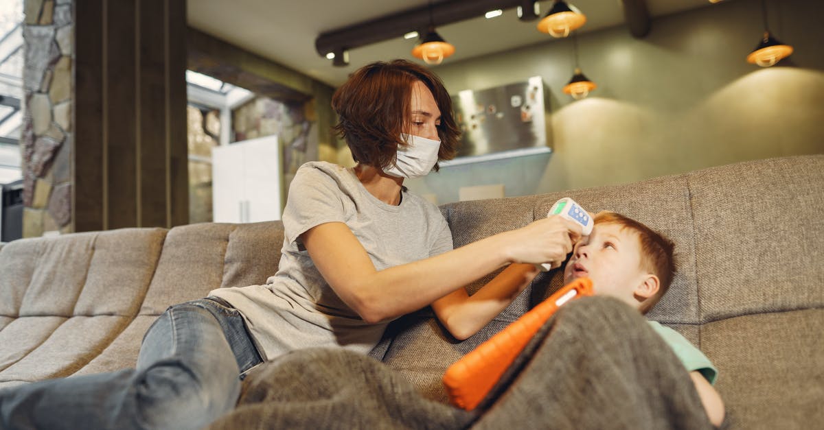 Infrared thermometer for oven temperatures - Low angle of slim mother in casual wear and face mask measuring boys body temperature using infrared thermometer while sitting on cozy sofa at home in afternoon during COVID 19 Infrared thermometer for oven temperatures - Low angle of slim mother in casual wear and face mask measuring boys body temperature using infrared thermometer while sitting on cozy sofa at home in afternoon during COVID 19