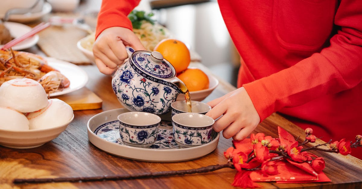 Infusing orange into tea while avoiding bitterness - Crop unrecognizable female pouring hot beverage from ornamental teapot into cup at table with oriental dishes in house Infusing orange into tea while avoiding bitterness - Crop unrecognizable female pouring hot beverage from ornamental teapot into cup at table with oriental dishes in house