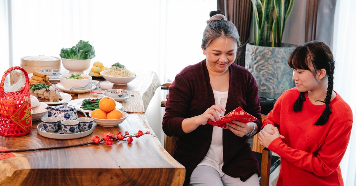 Infusing orange into tea while avoiding bitterness - Asian grandma with envelope against granddaughter during New Year holiday Infusing orange into tea while avoiding bitterness - Asian grandma with envelope against granddaughter during New Year holiday