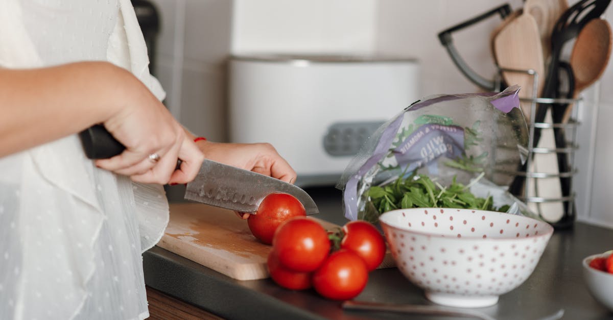 Ingredient selection for Canadian Poutine dish - Crop anonymous housewife in casual clothes cutting fresh ripe tomatoes with sharp knife on wooden cutting board while cooking in kitchen Ingredient selection for Canadian Poutine dish - Crop anonymous housewife in casual clothes cutting fresh ripe tomatoes with sharp knife on wooden cutting board while cooking in kitchen