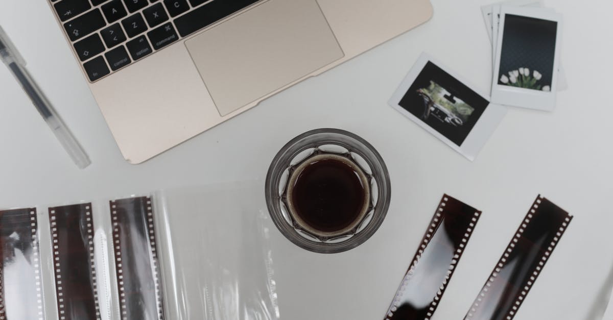 Instant coffee with only milk? - Top view of coffee cup with vintage instant photos and negative film strips placed on table with opened laptop Instant coffee with only milk? - Top view of coffee cup with vintage instant photos and negative film strips placed on table with opened laptop