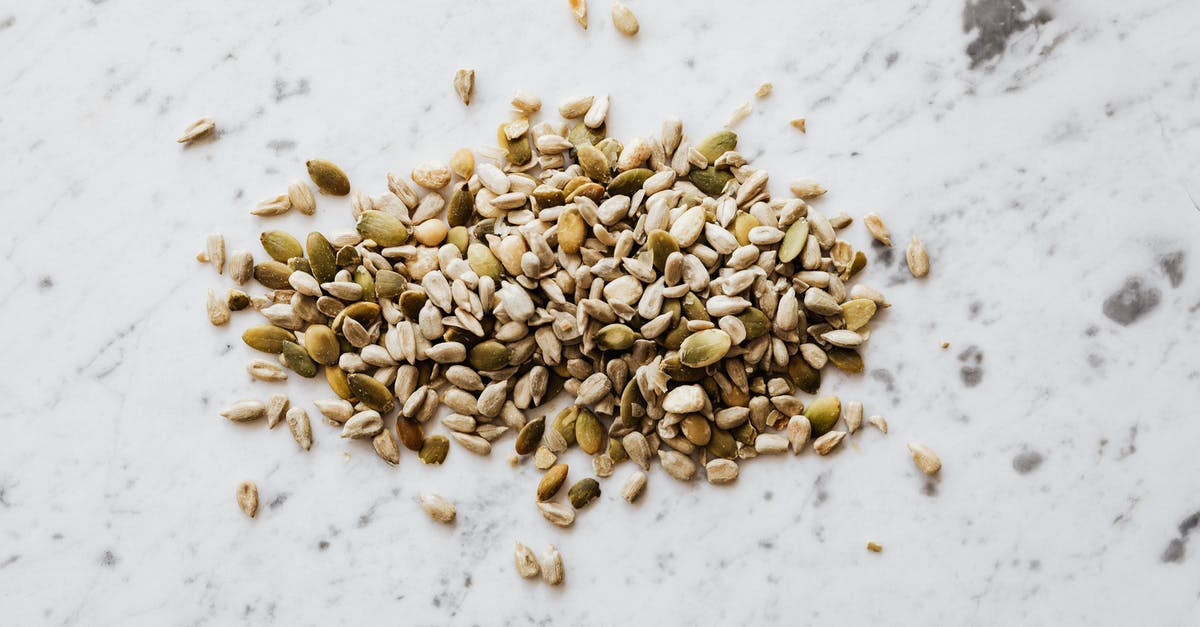 Is a seed different from a nut? - From above of oval shaped dried pumpkin seeds with green and gray shell spilled on marble surface with spots Is a seed different from a nut? - From above of oval shaped dried pumpkin seeds with green and gray shell spilled on marble surface with spots