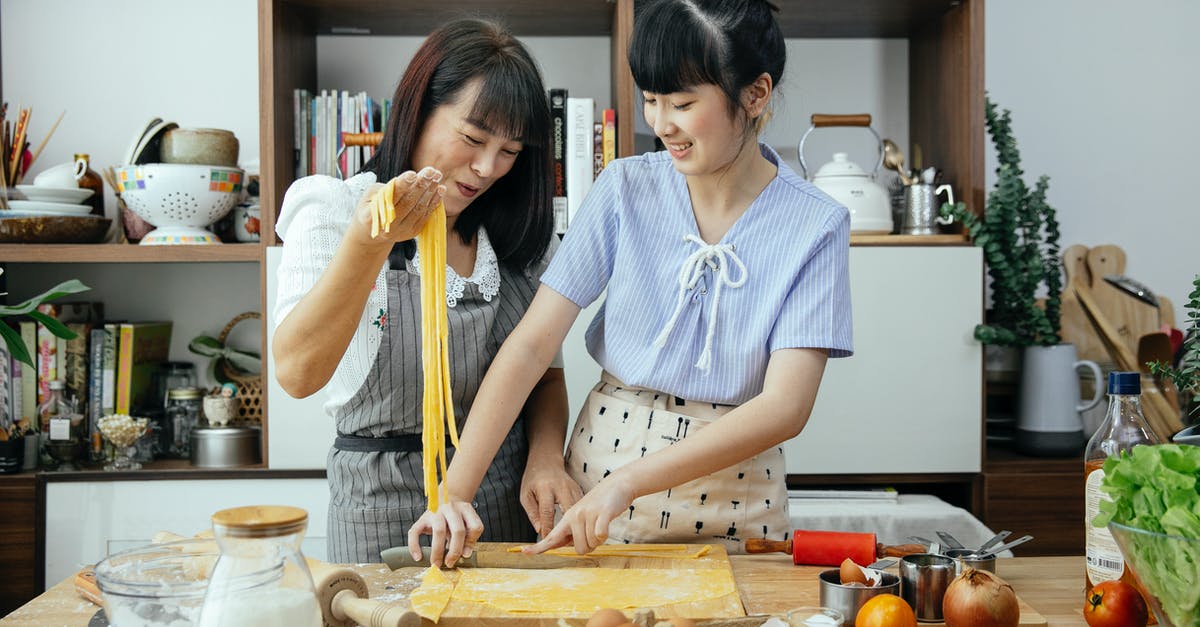 Is eating uncooked spaghetti dangerous? - Smiling women making noodles in kitchen Is eating uncooked spaghetti dangerous? - Smiling women making noodles in kitchen