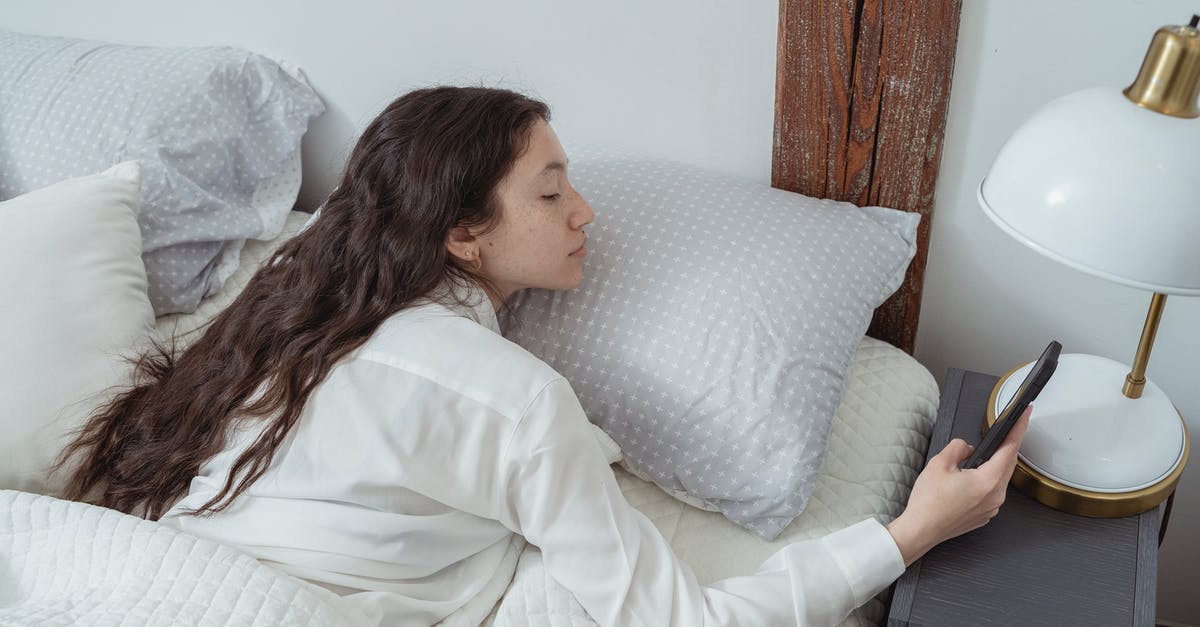 Is it better to use soft or hard ladyfingers when making tiramisu? - Side view of young brunette with long hair in white nightwear lying on belly in comfortable bed under blanket and using mobile phone in morning at home