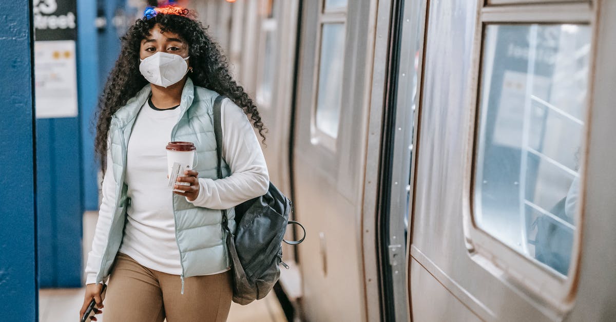 Is it safe to drink the whey? - Calm black woman with coffee wearing medical mask standing in metro Is it safe to drink the whey? - Calm black woman with coffee wearing medical mask standing in metro