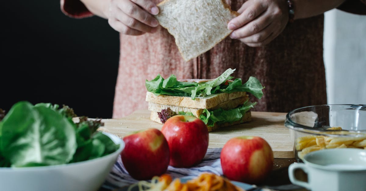 Is it safe to eat an apple cooked inside poultry? - Unrecognizable female cook putting slice of bread on lettuce while standing at table and making sandwich in kitchen during breakfast time Is it safe to eat an apple cooked inside poultry? - Unrecognizable female cook putting slice of bread on lettuce while standing at table and making sandwich in kitchen during breakfast time