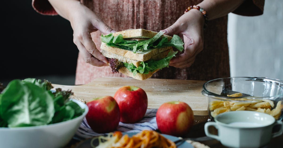Is it safe to eat an apple cooked inside poultry? - Unrecognizable female standing at table with apples and cutting board with sandwich with lettuce in hands in kitchen on breakfast time Is it safe to eat an apple cooked inside poultry? - Unrecognizable female standing at table with apples and cutting board with sandwich with lettuce in hands in kitchen on breakfast time