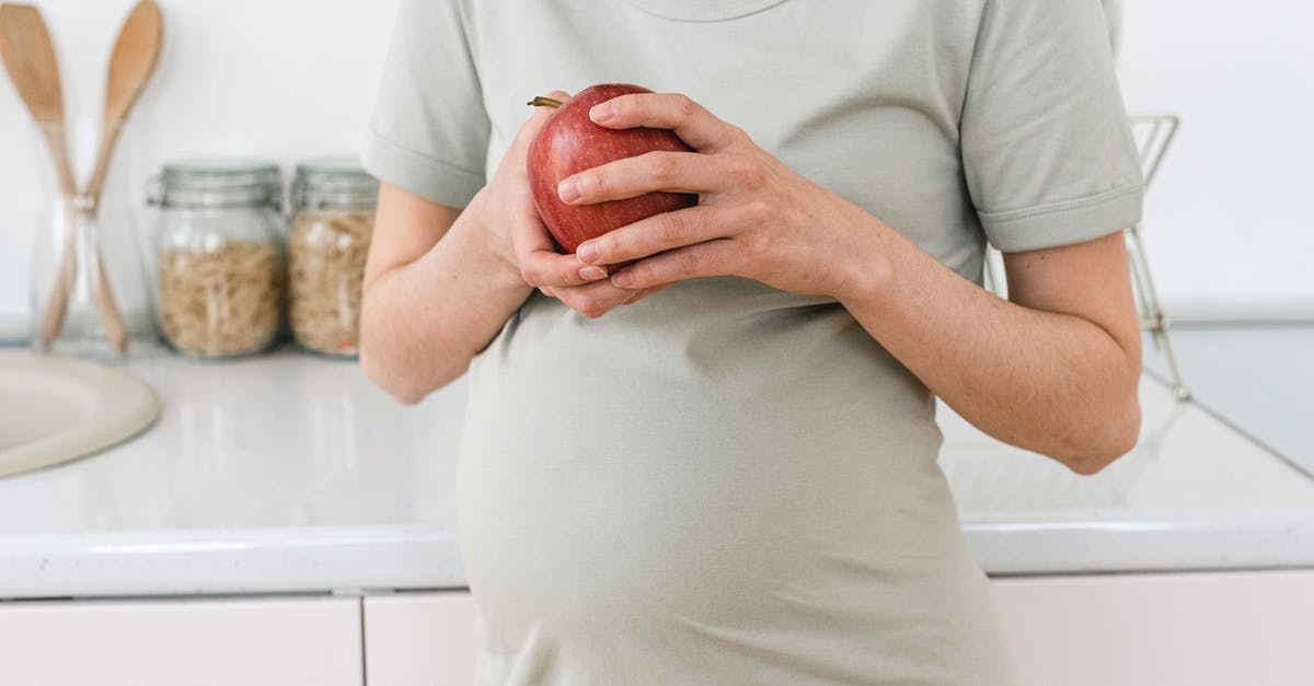 Is it safe to eat an apple cooked inside poultry? - Unrecognizable pregnant female with ripe red apple for healthy diet in hands standing near counter in light kitchen at home Is it safe to eat an apple cooked inside poultry? - Unrecognizable pregnant female with ripe red apple for healthy diet in hands standing near counter in light kitchen at home