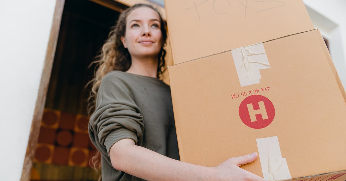 Is the grey stuff the thing we make fond out of - Confident young lady in casual wear carrying heavy carton boxes with toys and looking away while leaving old house