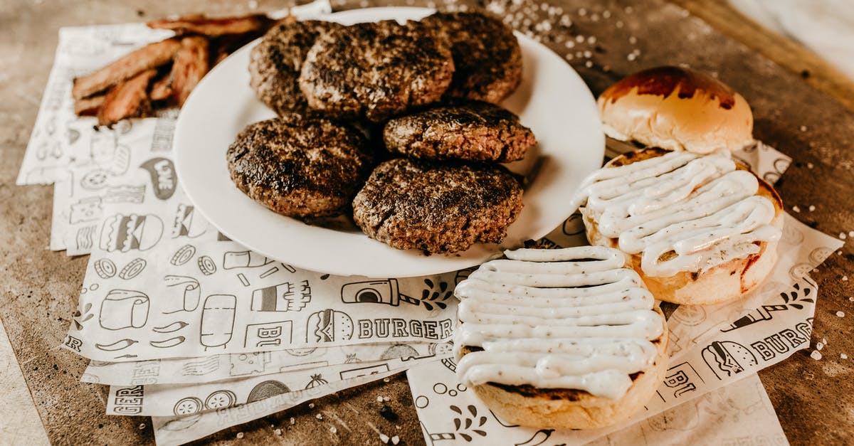 Is there a downside to tenderizing meat? - From above of bacon near plate with roasted appetizing patties for burgers and yummy golden bun on ornamental paper sheets on wooden table with sesame seeds