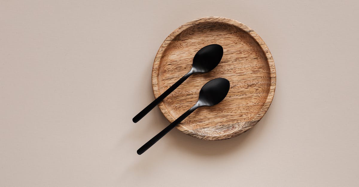 Is there a good, clean way to pit black olives? - Top view of composition of round wooden plate with smooth surface and similar black metal spoons on beige surface Is there a good, clean way to pit black olives? - Top view of composition of round wooden plate with smooth surface and similar black metal spoons on beige surface