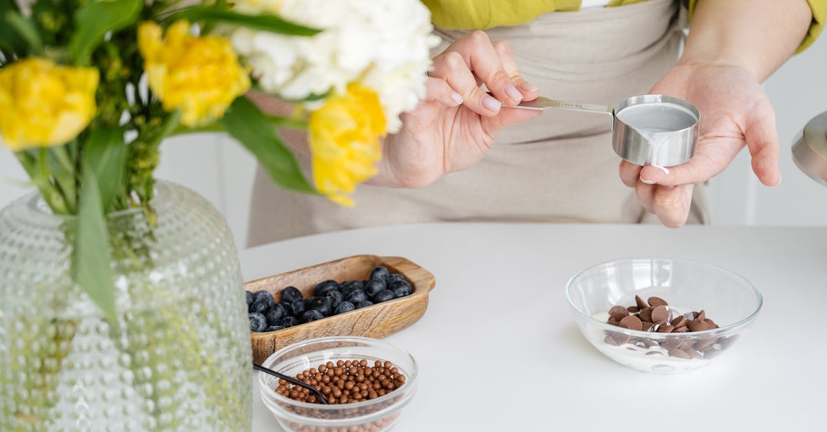Is there a sweet emulsion to put on oatmeal? - Crop faceless female confectioner wearing apron and casual clothes adding hot ganache made of heavy cream from saucepan into chocolate drops in glass bowl
