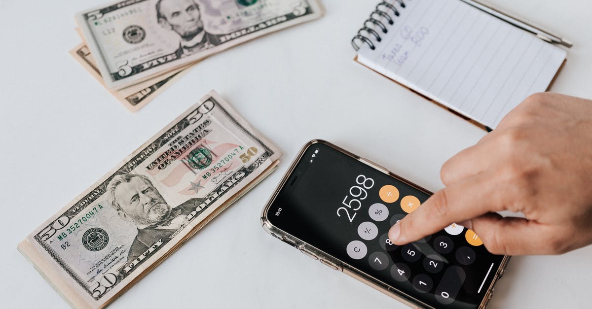 Is there an official comprehensive list of E-numbers? - From above of crop anonymous economist calculating total amount of income using calculator app on cellphone near piles of greenbacks and notebook with pen