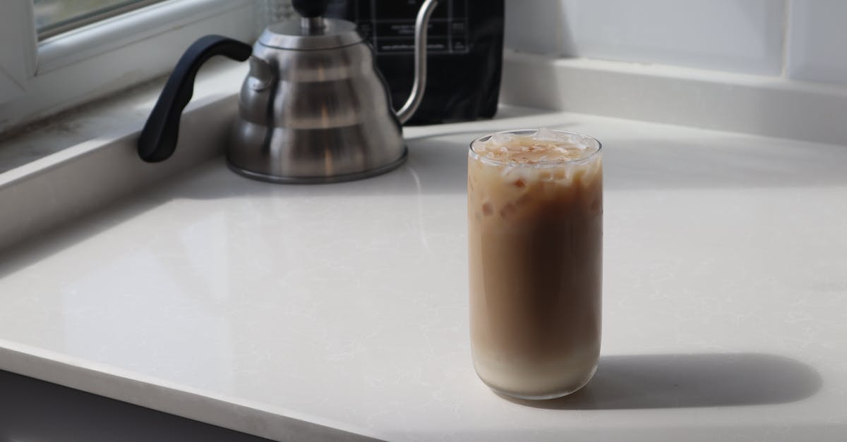 Is there any botulism risk in homemade cold brew coffee? - High angle glass of delicious iced latte and metal coffee kettle placed on white table in kitchen Is there any botulism risk in homemade cold brew coffee? - High angle glass of delicious iced latte and metal coffee kettle placed on white table in kitchen
