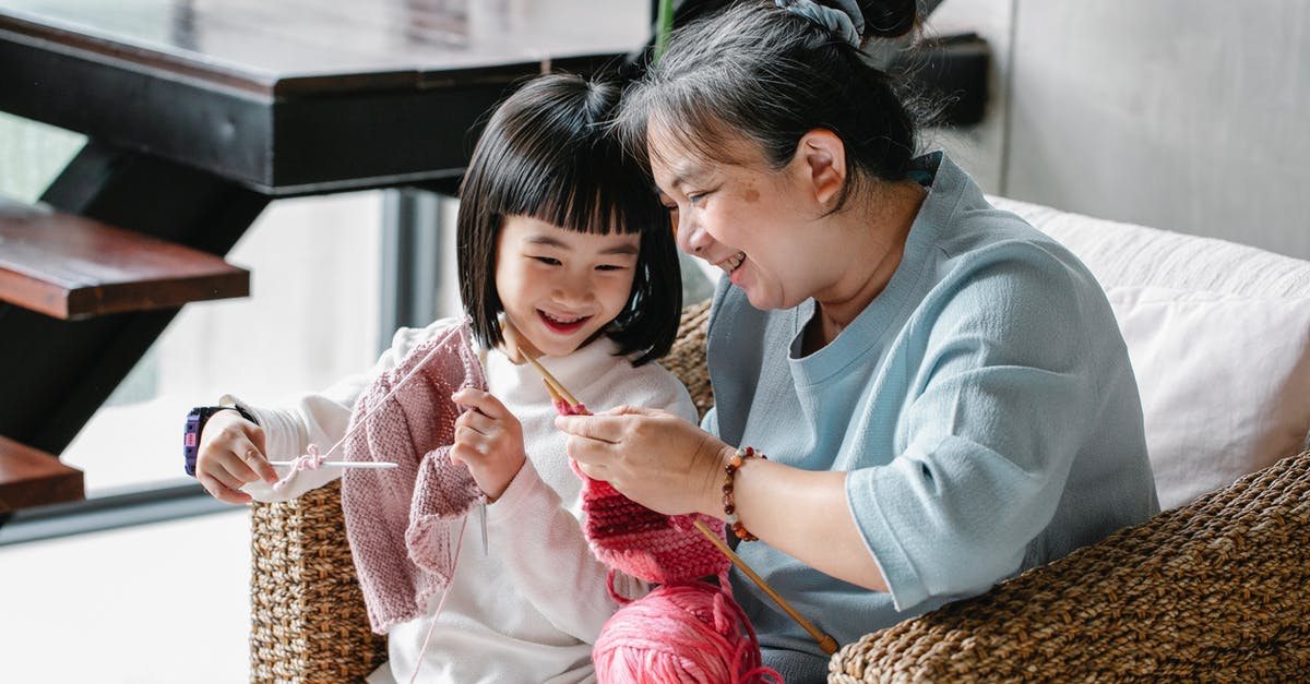 Is this some kind of warming oven? - Cheerful senior Asian woman sitting in armchair and helping curious little granddaughter to knit warm clothes with yarn in daylight Is this some kind of warming oven? - Cheerful senior Asian woman sitting in armchair and helping curious little granddaughter to knit warm clothes with yarn in daylight