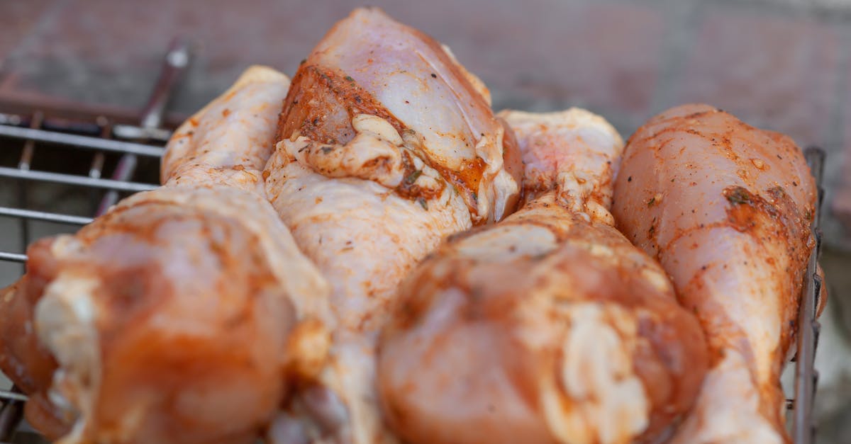 Keep chicken with skin from catching on fire on the barbeque - From above of raw chicken legs with seasoning placed on metal grill grate in daylight Keep chicken with skin from catching on fire on the barbeque - From above of raw chicken legs with seasoning placed on metal grill grate in daylight