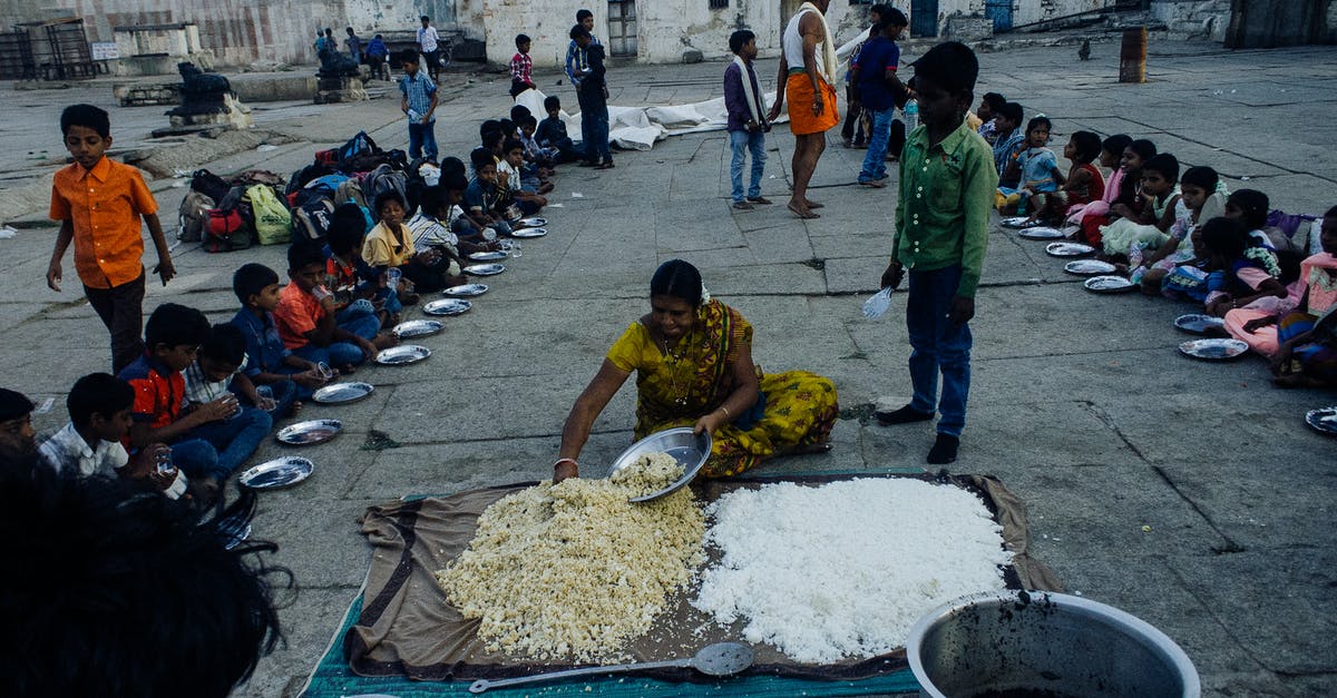 Keeping bugs out of rice - From above of old Indian woman serving food on plates while sitting on ground surrounded with kids in poor area Keeping bugs out of rice - From above of old Indian woman serving food on plates while sitting on ground surrounded with kids in poor area