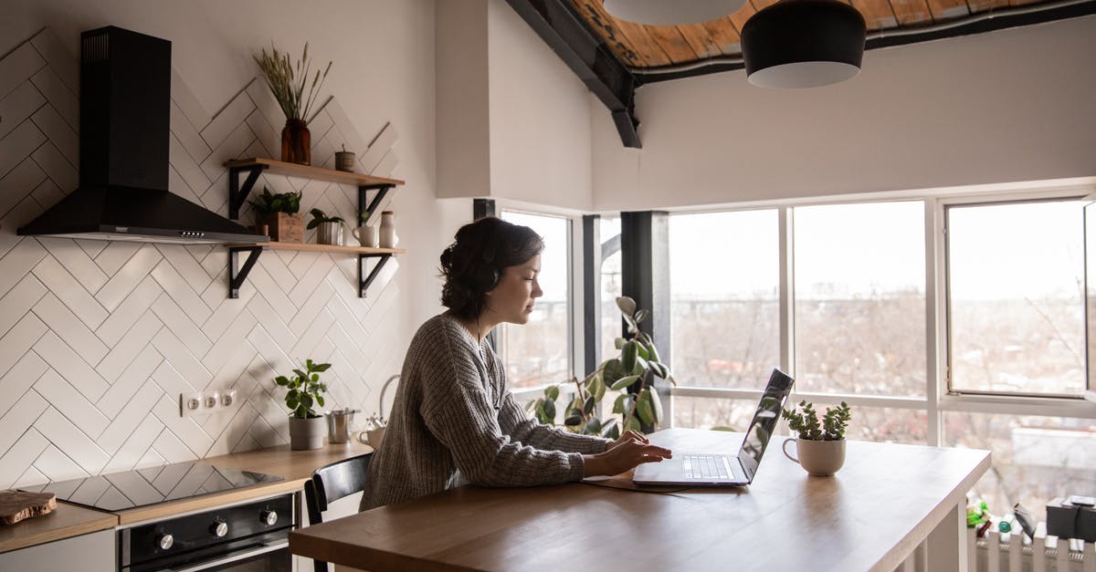 Kitchen clambake using kombu? - Side view of young female in casual clothes typing message on laptop while sitting at wooden table in kitchen Kitchen clambake using kombu? - Side view of young female in casual clothes typing message on laptop while sitting at wooden table in kitchen