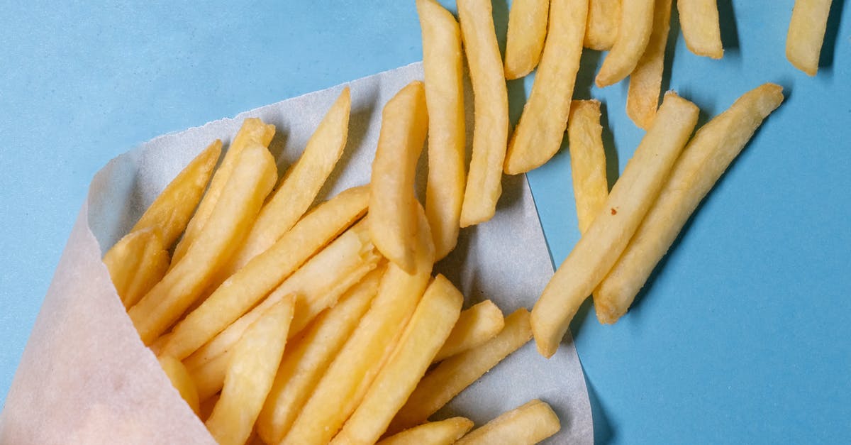 Low-calorie French Fries - Top view of tasty french fries in paper placed on blue table in light studio Low-calorie French Fries - Top view of tasty french fries in paper placed on blue table in light studio