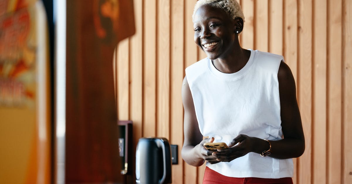 Make espresso in office kitchen- just have a kettle and microwave? - Young happy black woman using smartphone in office kitchen Make espresso in office kitchen- just have a kettle and microwave? - Young happy black woman using smartphone in office kitchen