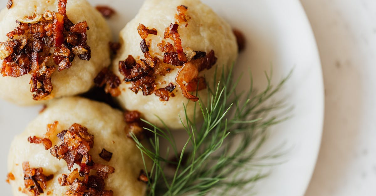 Making a test tiny roast - Top view closeup of white ceramic plate with Lithuanian potato cepelinai with fried bacon bits on top and fresh dill sprig aside on marble table
