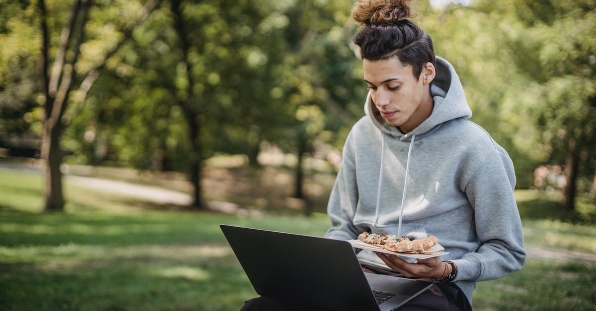 Making cookies on a pizza stone - Young concentrated man surfing netbook while preparing for exams and eating pizza in park Making cookies on a pizza stone - Young concentrated man surfing netbook while preparing for exams and eating pizza in park