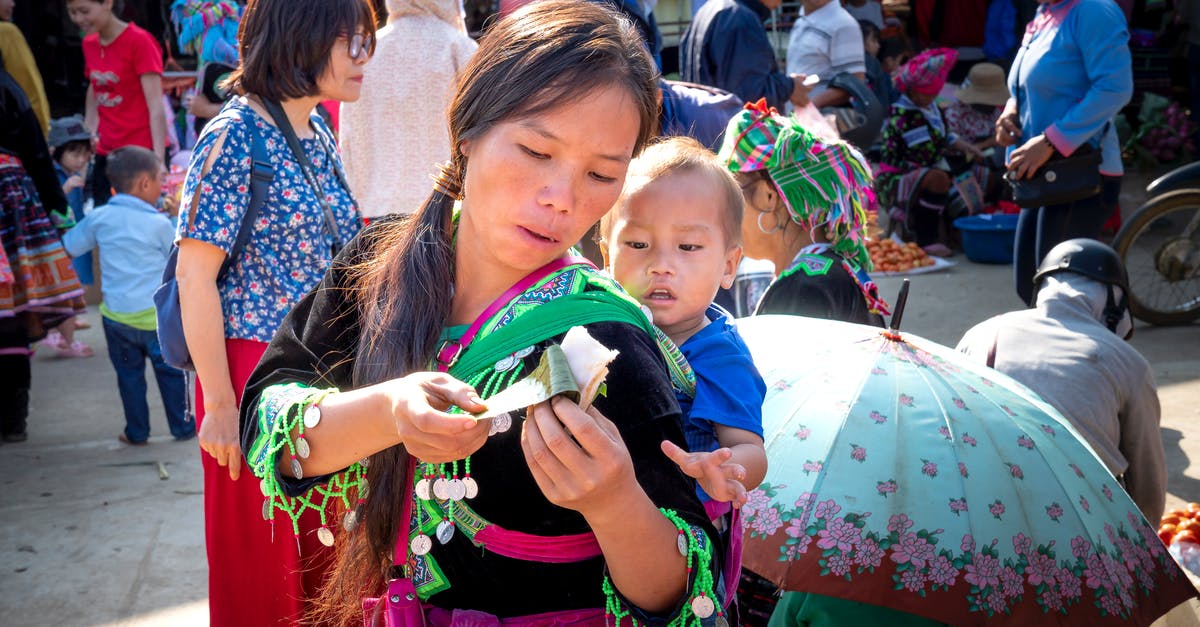 Making sticky rice without rice cooker - Young ethnic mom in traditional wear with baby and sticky rice in banana leaf in urban market Making sticky rice without rice cooker - Young ethnic mom in traditional wear with baby and sticky rice in banana leaf in urban market