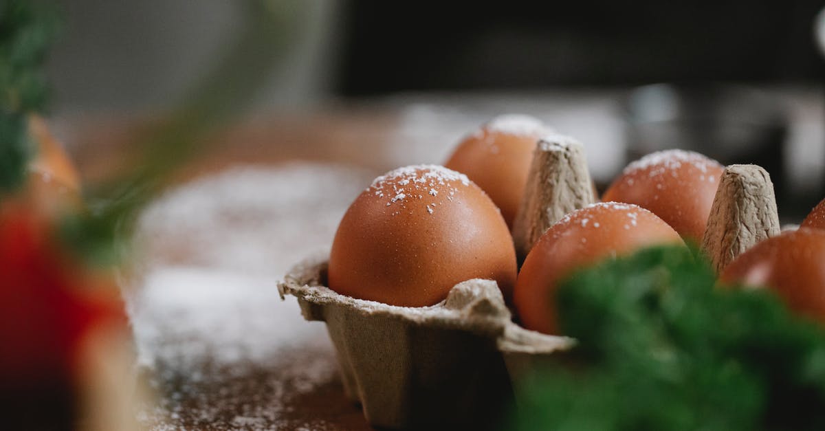 Meals to cook using a whole chicken - Uncooked chicken eggs in carton container with fresh greens placed on table with flour Meals to cook using a whole chicken - Uncooked chicken eggs in carton container with fresh greens placed on table with flour