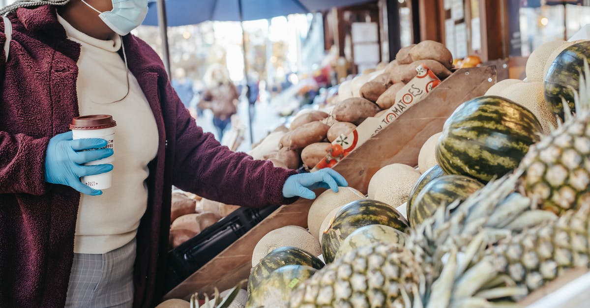 Melon buying tips - Side view of African American female in casual clothes medical mask and latex gloves buying melon in food shop on street Melon buying tips - Side view of African American female in casual clothes medical mask and latex gloves buying melon in food shop on street