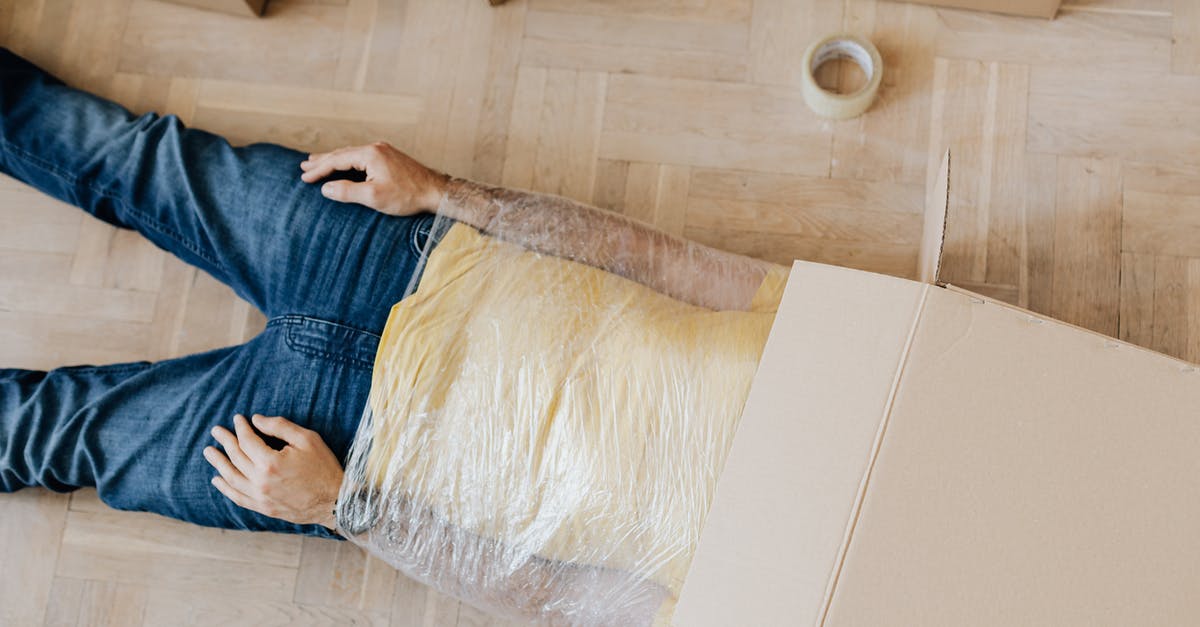 Melted plastic wrap in oven at high temp - From above anonymous male in casual clothing lying on parquet with box on head and upper body wrapped in clingy plastic tape during moving out Melted plastic wrap in oven at high temp - From above anonymous male in casual clothing lying on parquet with box on head and upper body wrapped in clingy plastic tape during moving out