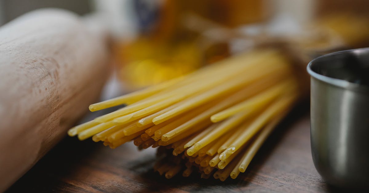 Metal cutlery food pairing - Bunch of uncooked spaghetti near metal bowl and rolling pin placed on wooden surface on light kitchen Metal cutlery food pairing - Bunch of uncooked spaghetti near metal bowl and rolling pin placed on wooden surface on light kitchen
