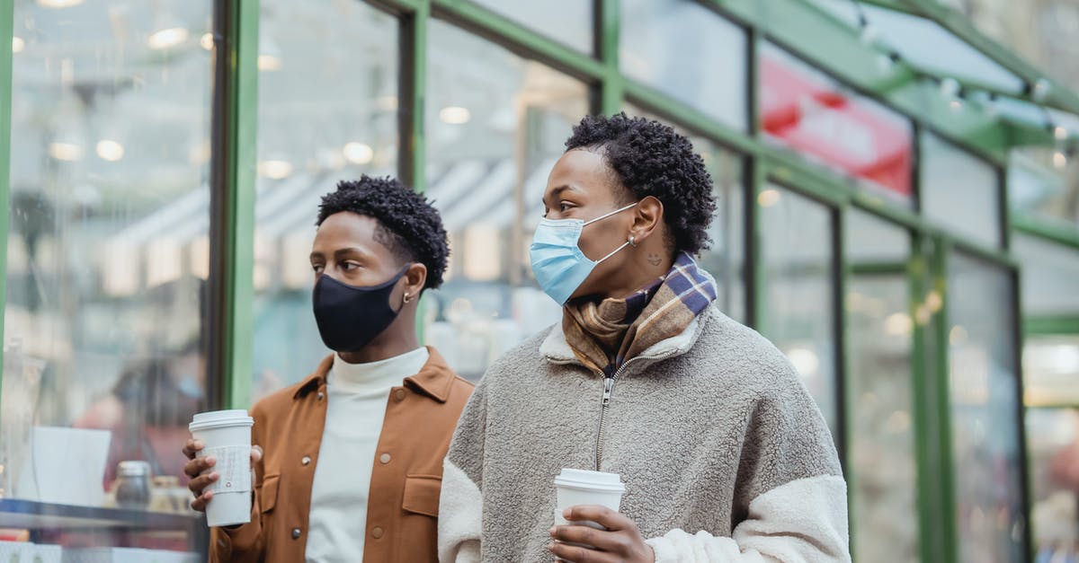Microwave-safe cups becoming less safe - African American male couple in protective masks walking on street along building with paper cups of takeaway beverages in city Microwave-safe cups becoming less safe - African American male couple in protective masks walking on street along building with paper cups of takeaway beverages in city