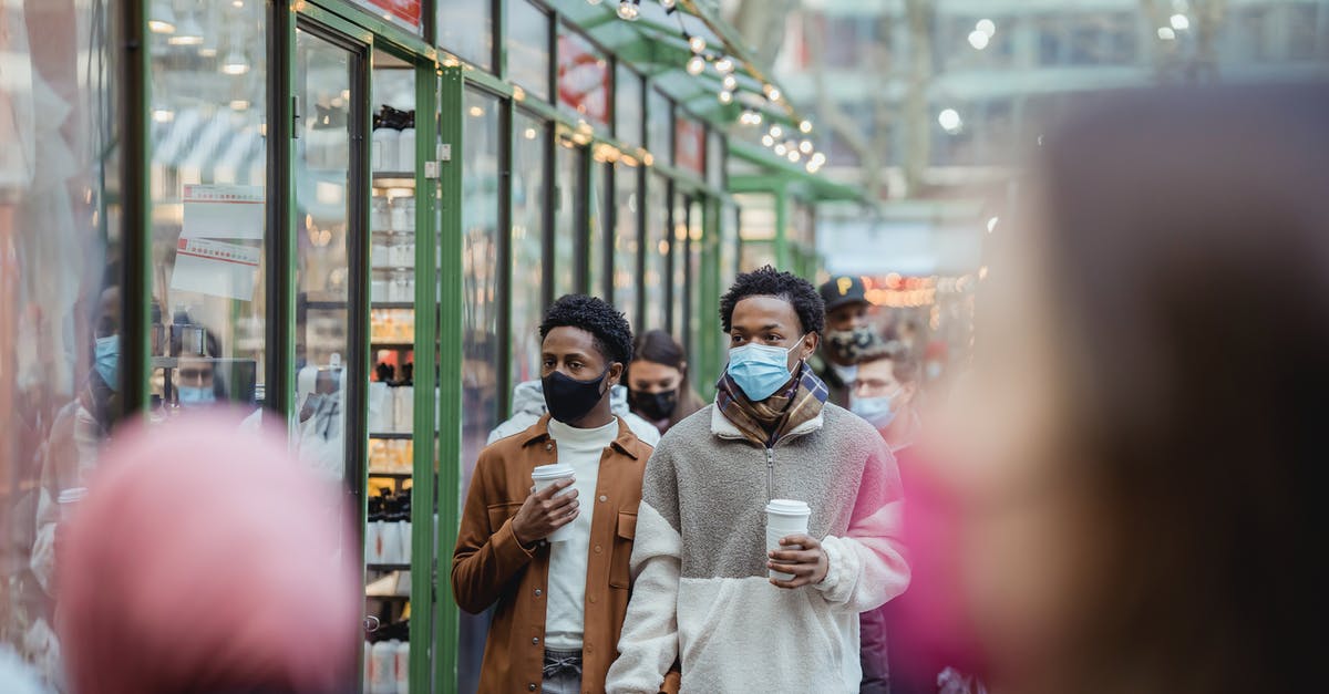 Microwave-safe cups becoming less safe - African American homosexual male in protective masks holding hands while strolling on street with takeaway coffee on street with people Microwave-safe cups becoming less safe - African American homosexual male in protective masks holding hands while strolling on street with takeaway coffee on street with people