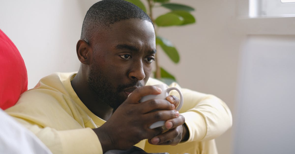 Minimum amount of oil that should be used in deep fryer - Attentive black man drinking coffee against laptop on bed Minimum amount of oil that should be used in deep fryer - Attentive black man drinking coffee against laptop on bed