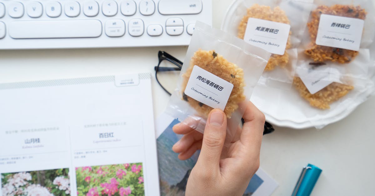 Name of a Chinese sweet - Top view of unrecognizable person taking cookie in transparent package with label while working at table with laptop and notebook Name of a Chinese sweet - Top view of unrecognizable person taking cookie in transparent package with label while working at table with laptop and notebook