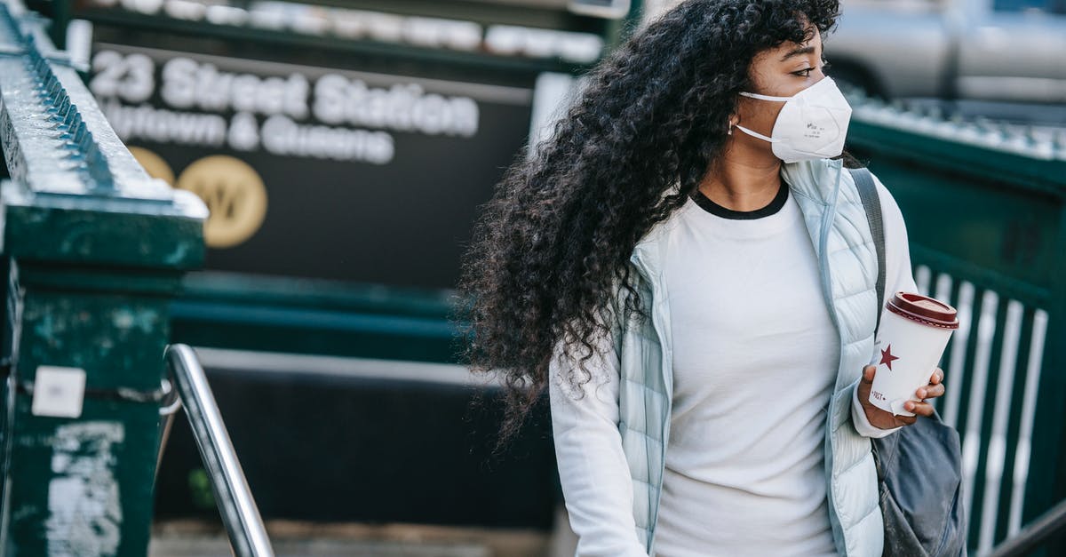 Normal coffee vs decaf - Emotionless African American female with coffee to go wearing casual wear and protective face mask leaving underground station and looking away in New York City Normal coffee vs decaf - Emotionless African American female with coffee to go wearing casual wear and protective face mask leaving underground station and looking away in New York City