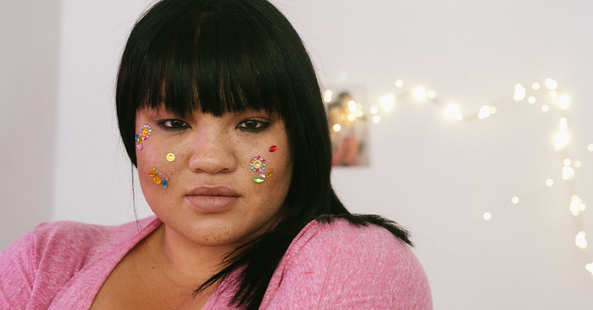 Not a tender steak - Tender young ethnic overweight lady with black hair and colourful glitter on face wearing pink shirt standing in light decorated room and looking at camera Not a tender steak - Tender young ethnic overweight lady with black hair and colourful glitter on face wearing pink shirt standing in light decorated room and looking at camera