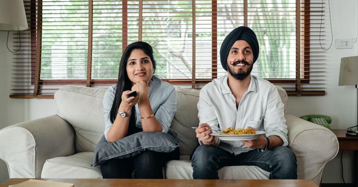 Nuke TV Dinner and then renuke it 3 hours later? - Positive male with plate of food and female in casual clothes sitting on sofa in living room and watching TV at home Nuke TV Dinner and then renuke it 3 hours later? - Positive male with plate of food and female in casual clothes sitting on sofa in living room and watching TV at home