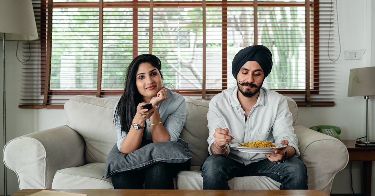 Nuke TV Dinner and then renuke it 3 hours later? - Pensive Indian male having meal on sofa while woman female in casual clothes sitting near and switching TV channels Nuke TV Dinner and then renuke it 3 hours later? - Pensive Indian male having meal on sofa while woman female in casual clothes sitting near and switching TV channels