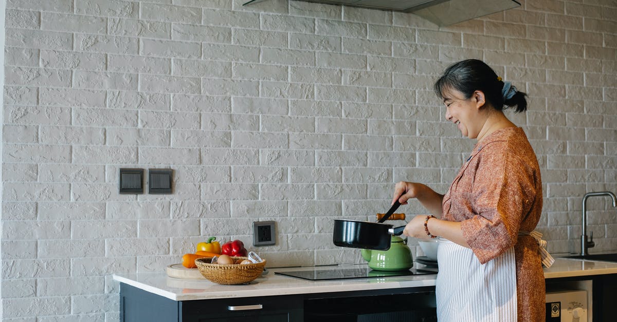 Old recipe conversions - Side view of elderly female in apron standing near stove and holding pan while preparing lunch at home Old recipe conversions - Side view of elderly female in apron standing near stove and holding pan while preparing lunch at home