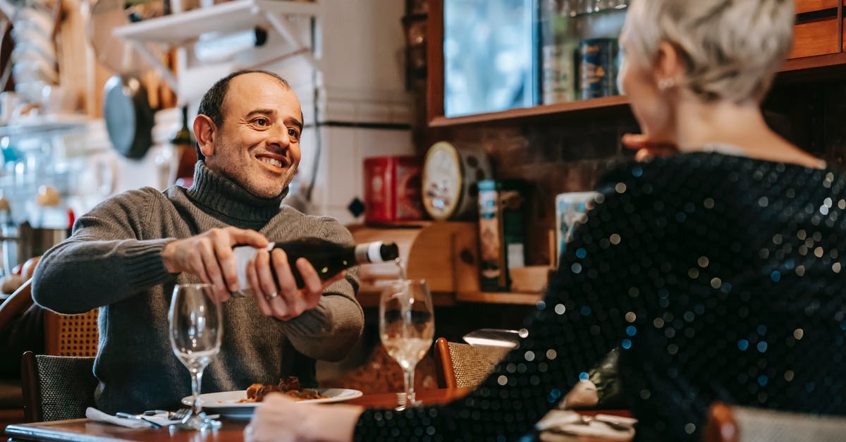 Opening wine bottle with rounded top using a waiter's friend - Positive couple having date at table while man pouring wine from bottle into wineglasses near plates with tasty dish in bright restaurant while looking at each other Opening wine bottle with rounded top using a waiter's friend - Positive couple having date at table while man pouring wine from bottle into wineglasses near plates with tasty dish in bright restaurant while looking at each other