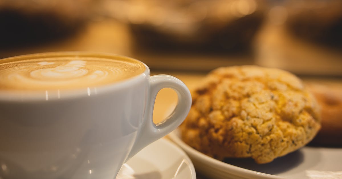 Oven baked cod fillets get soaked in their own liquid - Mug of tasty fragrant coffee with latte art served near plate with oatmeal cookies on table on blurred background Oven baked cod fillets get soaked in their own liquid - Mug of tasty fragrant coffee with latte art served near plate with oatmeal cookies on table on blurred background